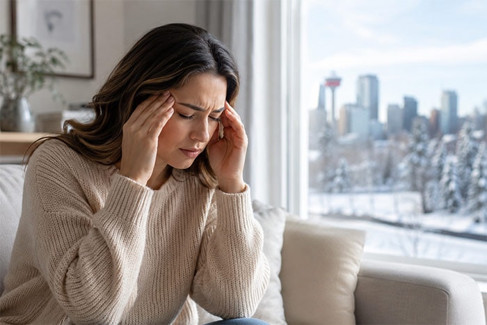 A woman holding her head in discomfort, representing Chinook-triggered headaches in Calgary
