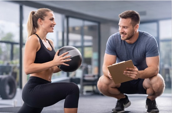 A female squatting with an exercise ball while a male squats in the gym