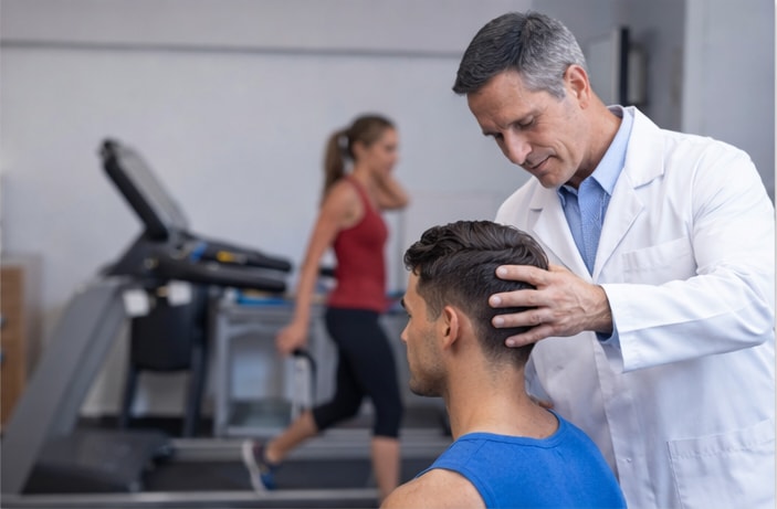 A chiropractor assessing the neck of an athlete in the gym